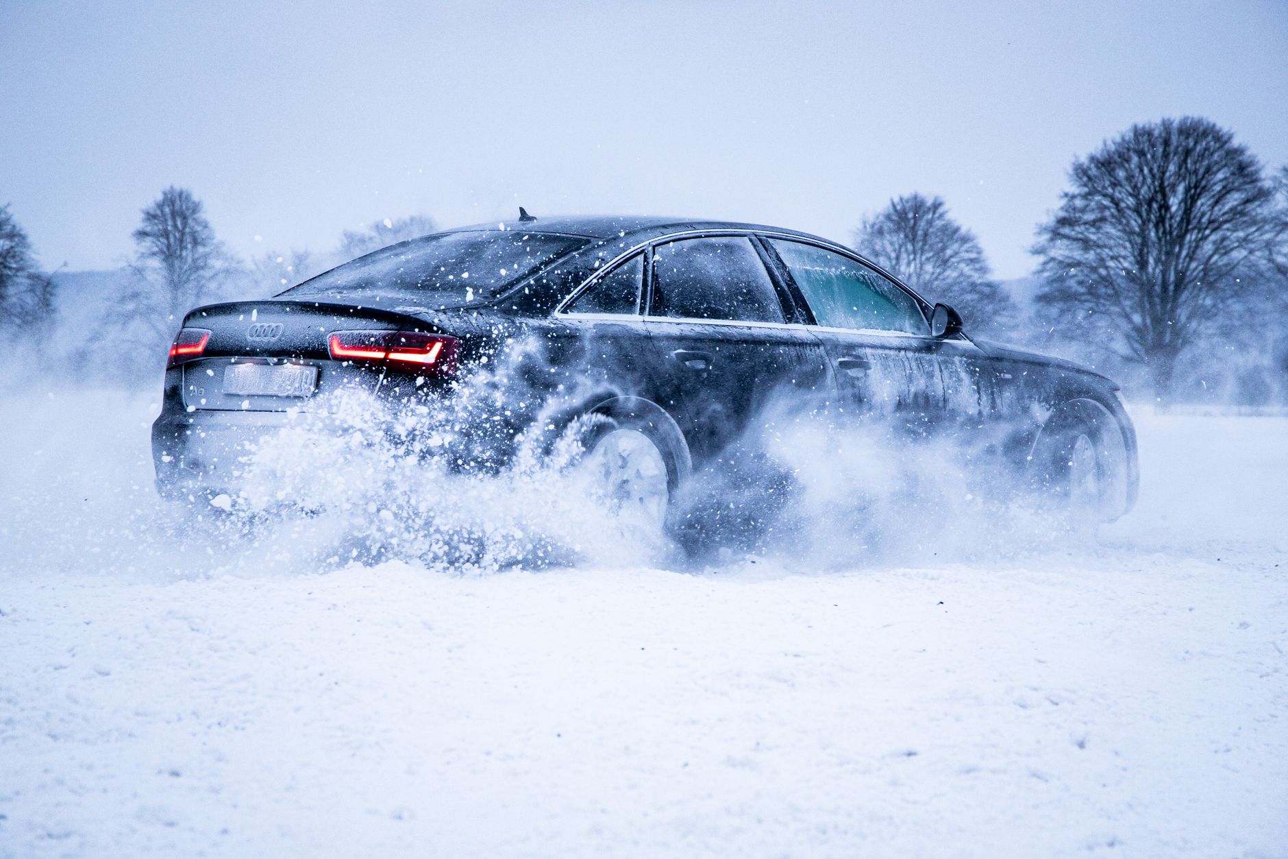 a black audi car driving on a snow covered field